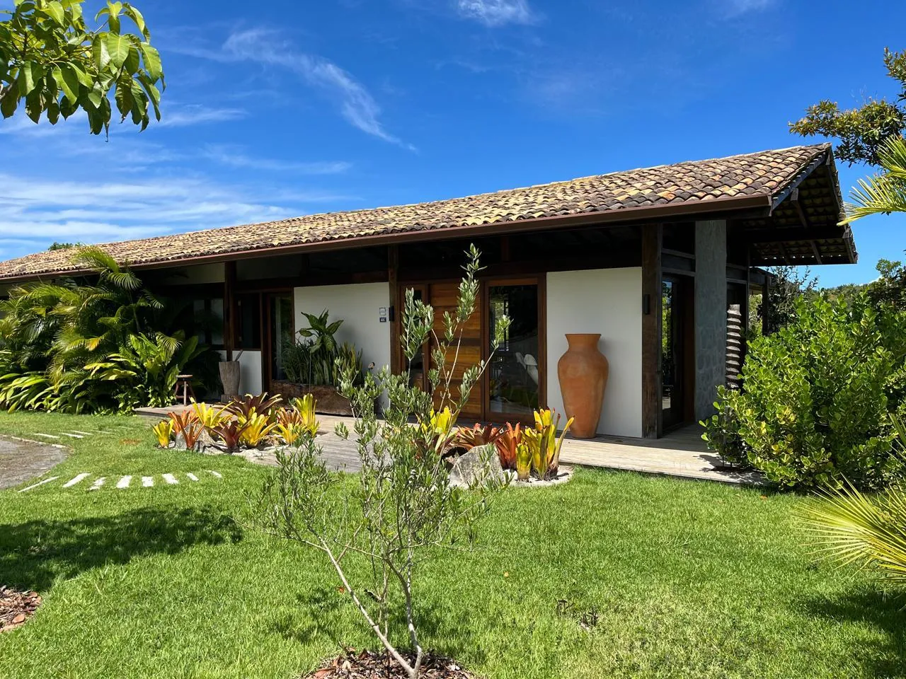 Casa com jardim tropical, gramado e canteiros de bromélias projetados pela Nicolai Jardins